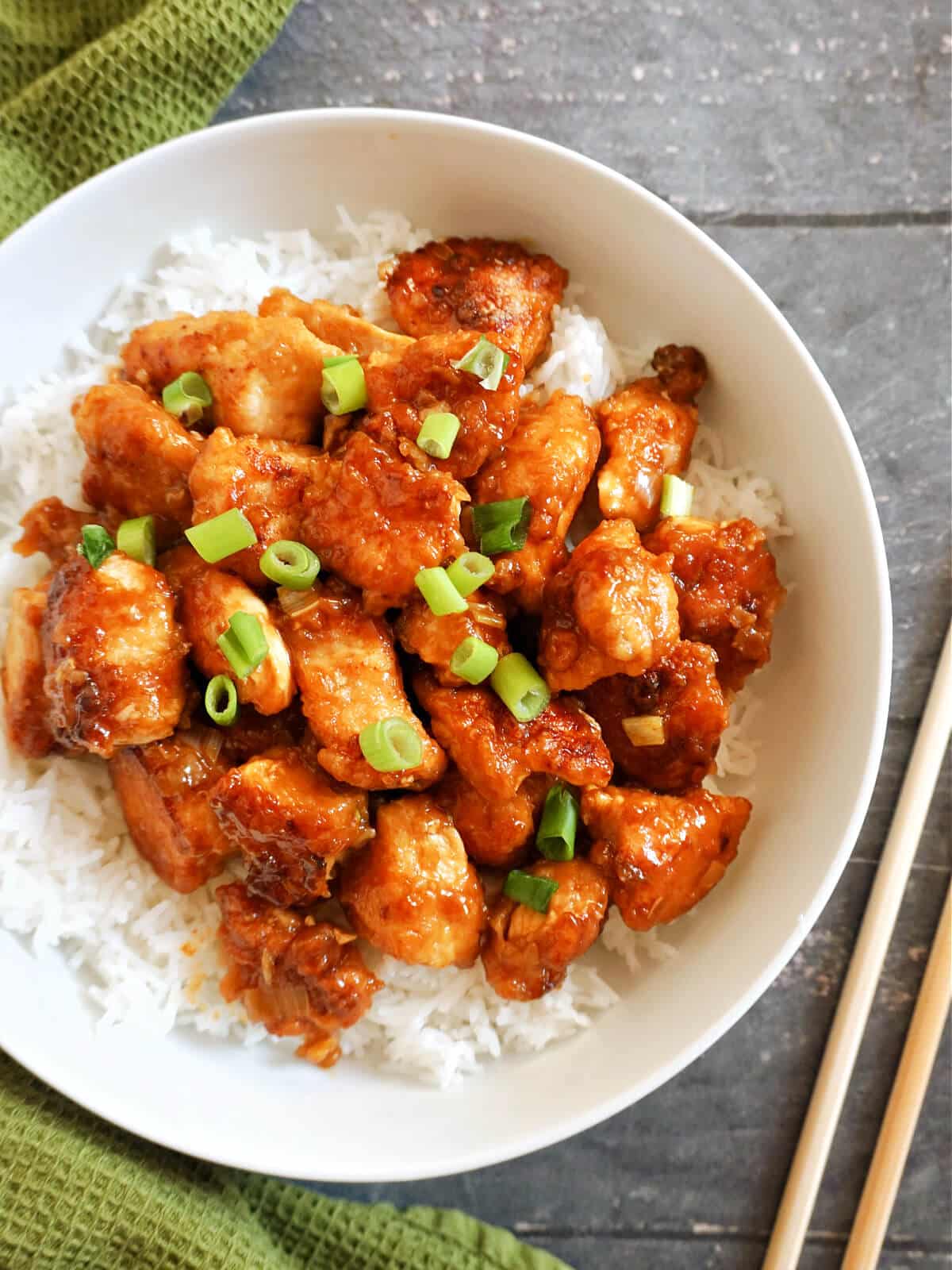 Overhead shoot of a white bowl with orange chicken pieces on a bed of rice.