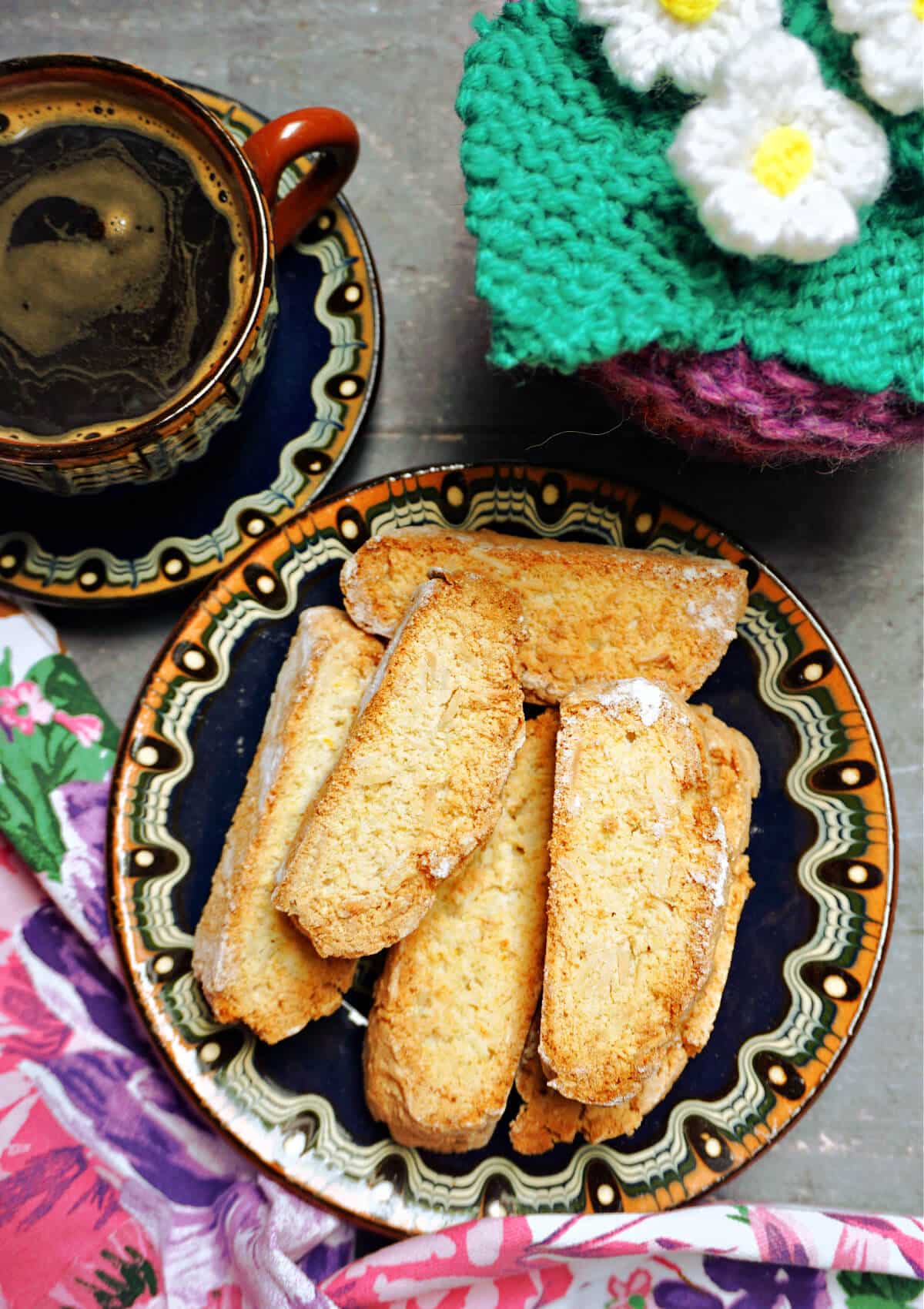 Overhead shoot of a plate with 5 biscotti, a cup of coffee next to it and a knitted flower pot.