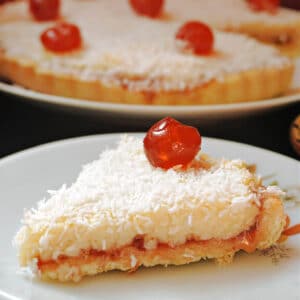 A slice of Manchester tart on a white plate with more tart in the background