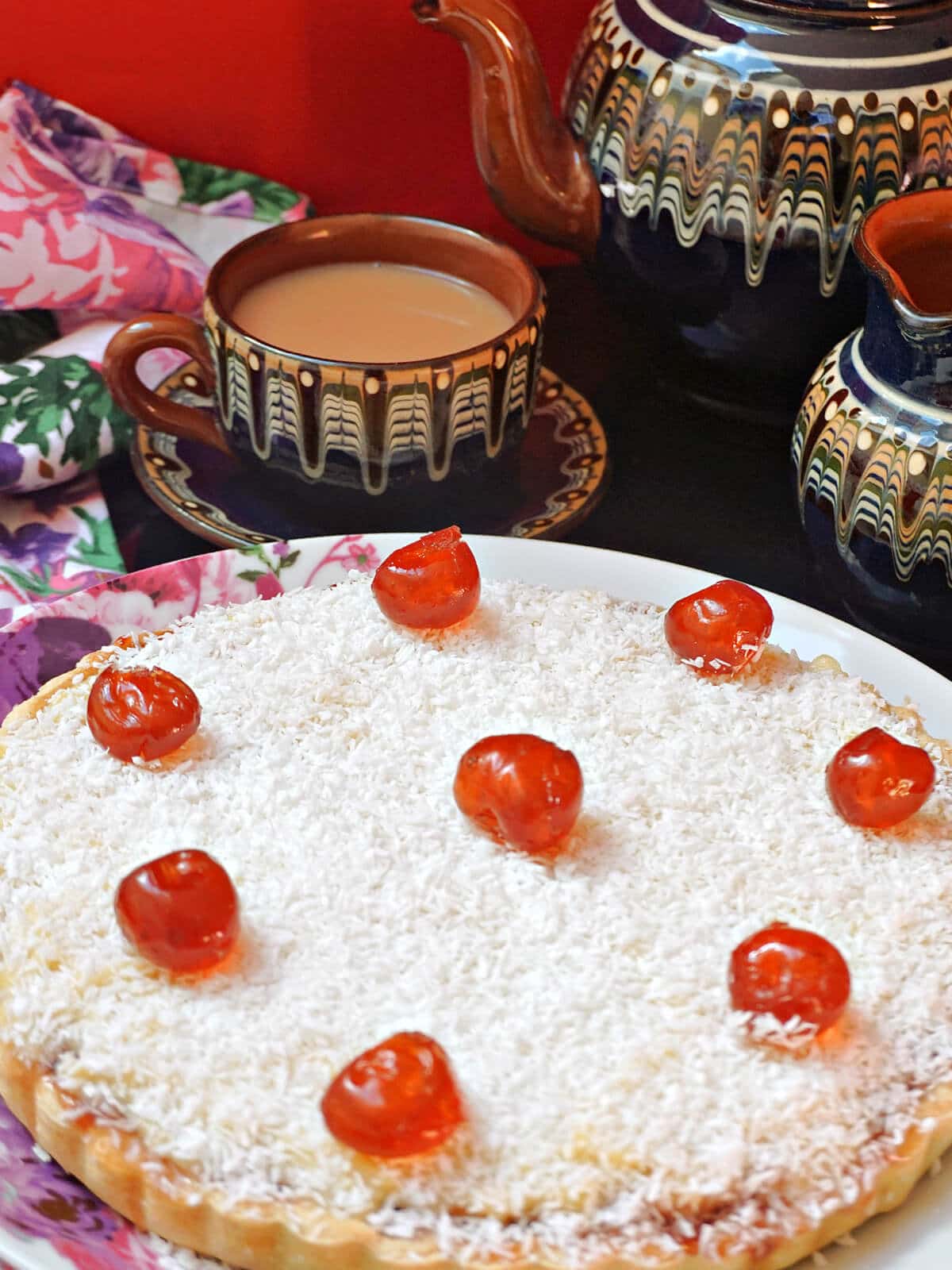 A tart on a white plate with a tea set in the background.