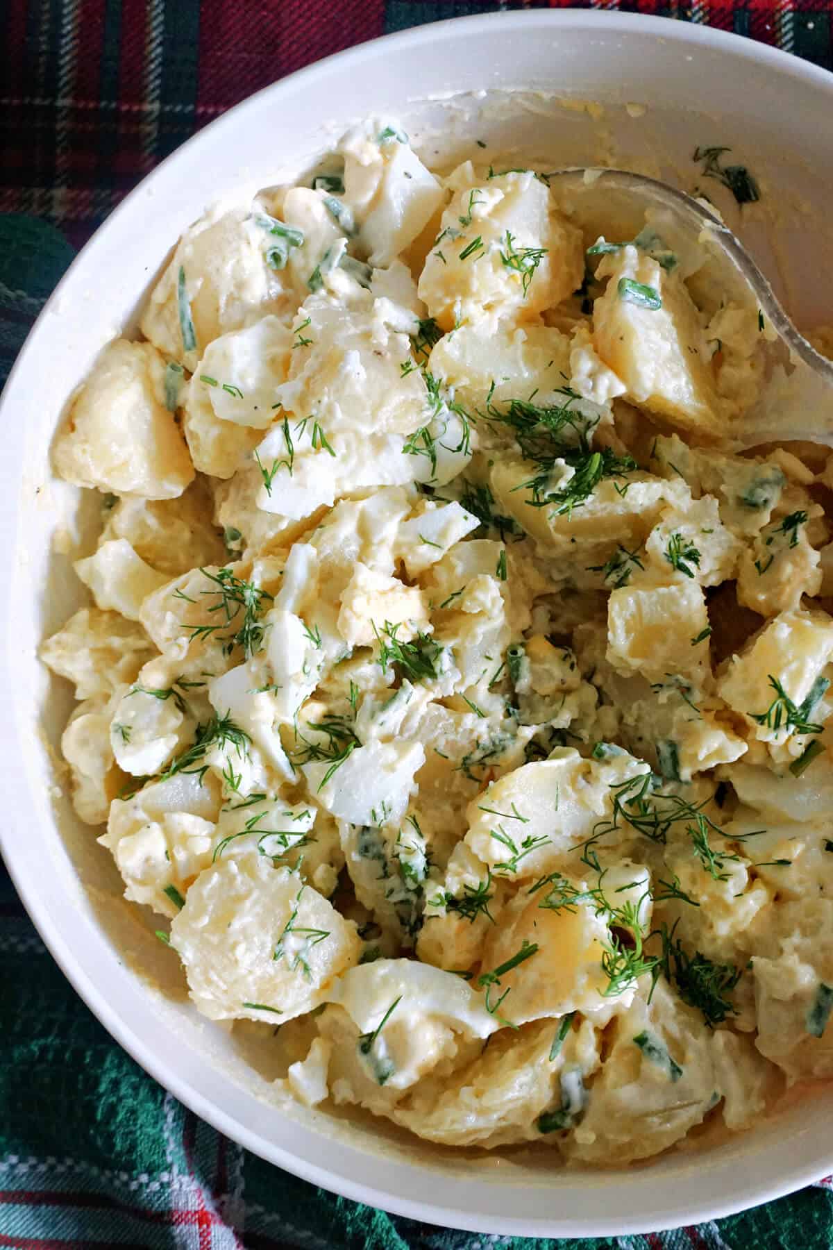 A white plate with potato and egg salad garnished with chopped dill.