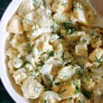 A white plate with potato egg salad garnished with fresh dill.