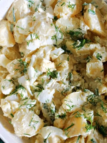 A white plate with potato egg salad garnished with fresh dill.