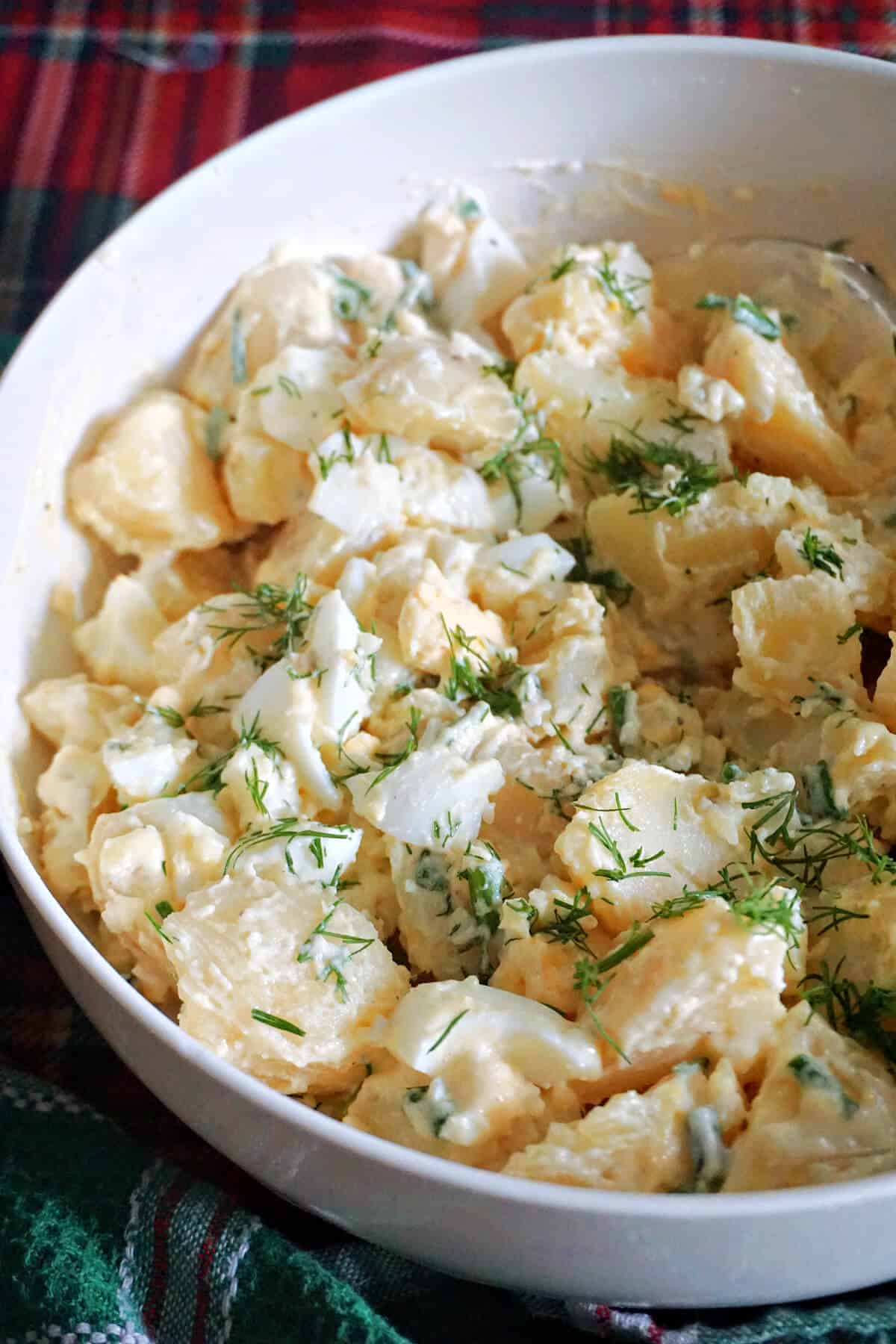 A white plate with a portion of potato and egg salad.