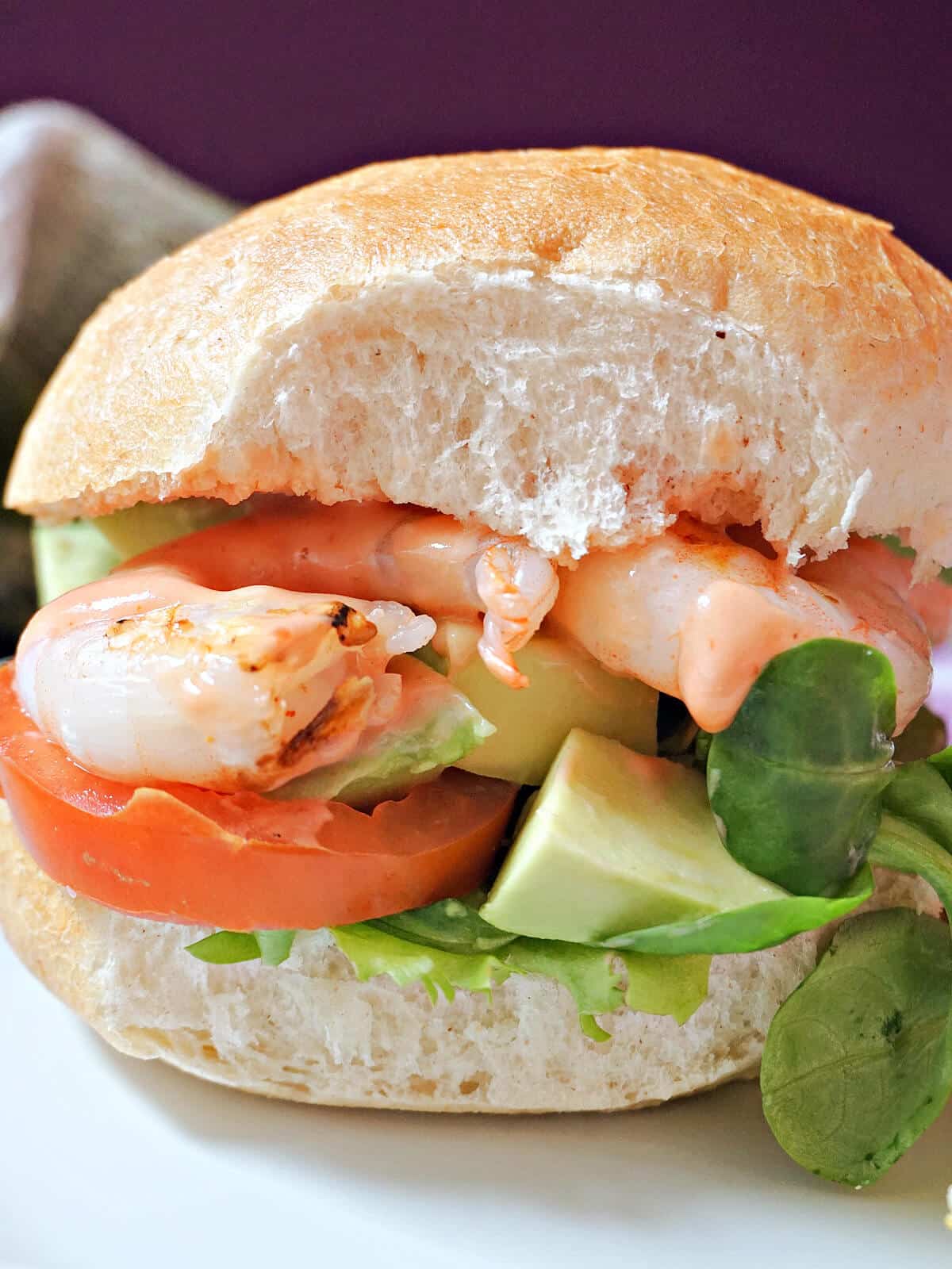 Close-up shoot of a prawn burger with avocado, tomatoes and salad.