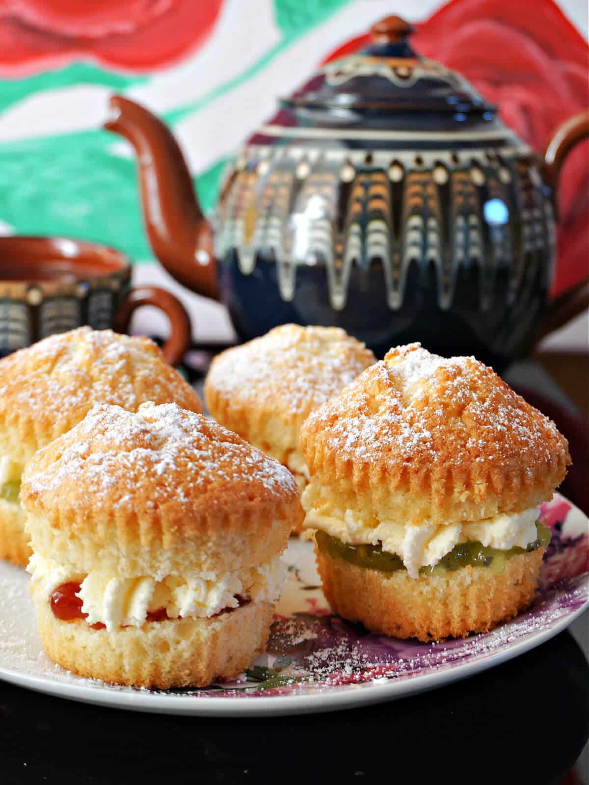 4 cupcakes on a white plate with a tea pot in the background