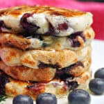 A pile of blueberry pancakes with blueberries around