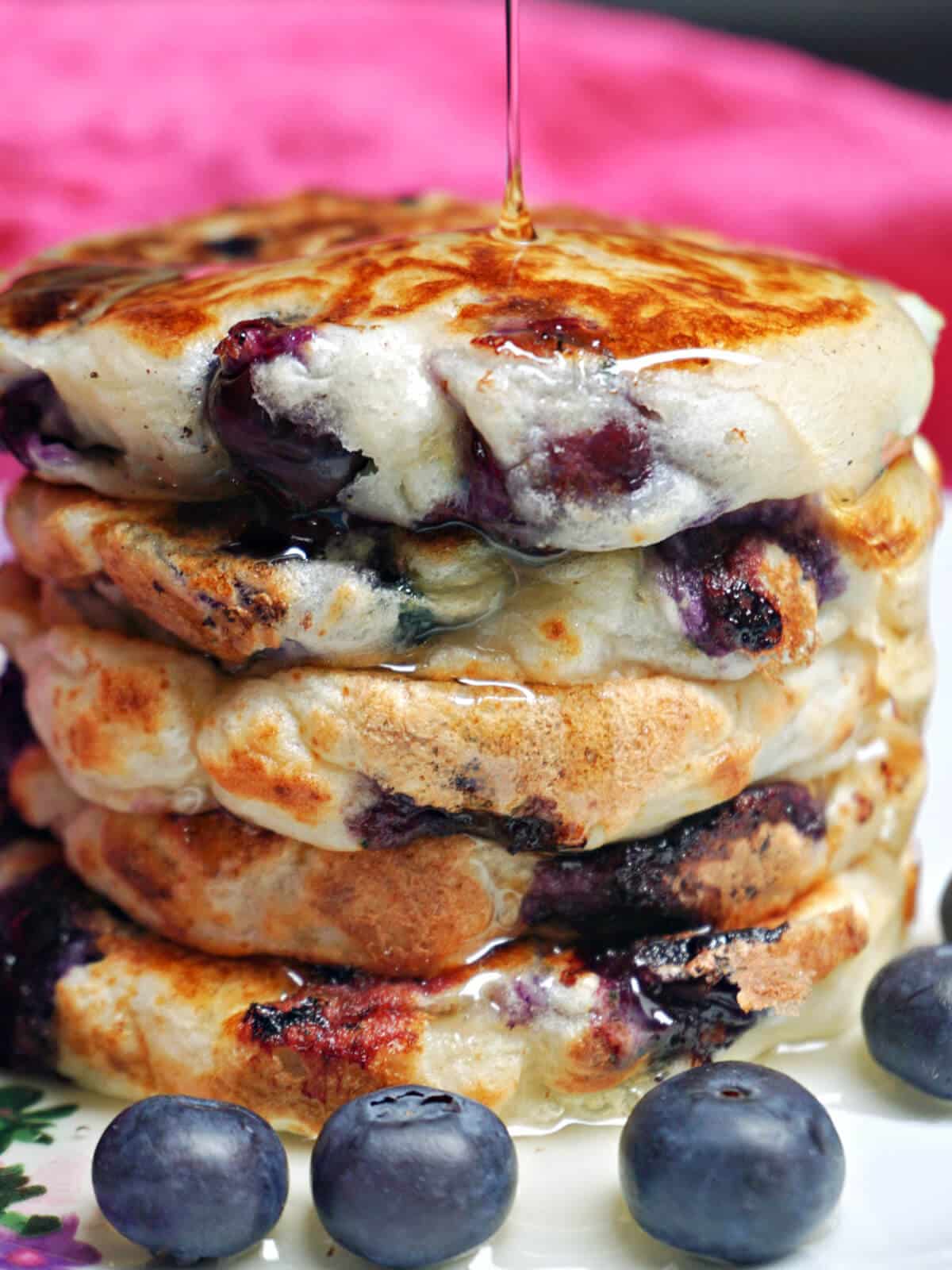 A pile of blueberry pancakes being drizzled with maple syrup.
