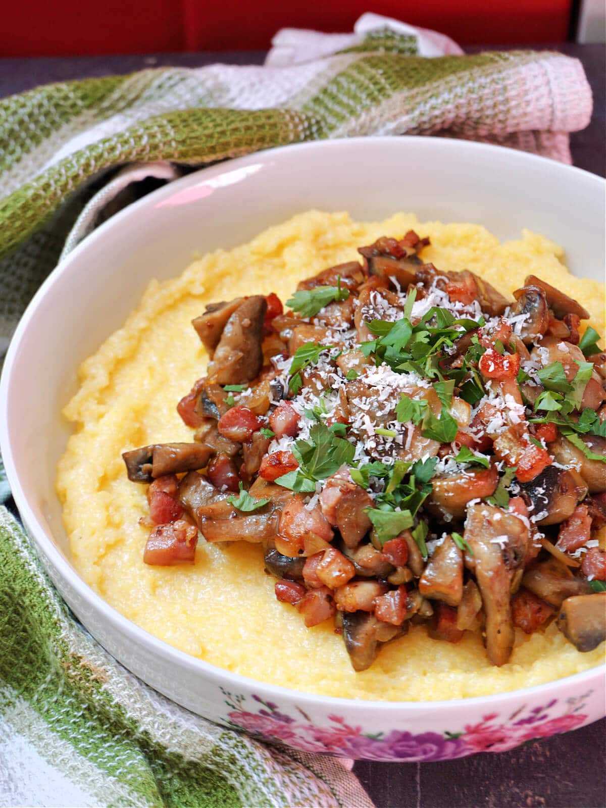 A white bowl with cooked mushrooms and bacon on a bed of polenta.