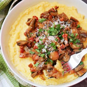 A white bowl with polenta topped with mushrooms and bacon