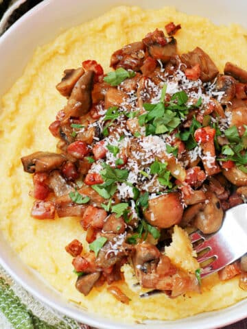 A white bowl with polenta topped with mushrooms and bacon