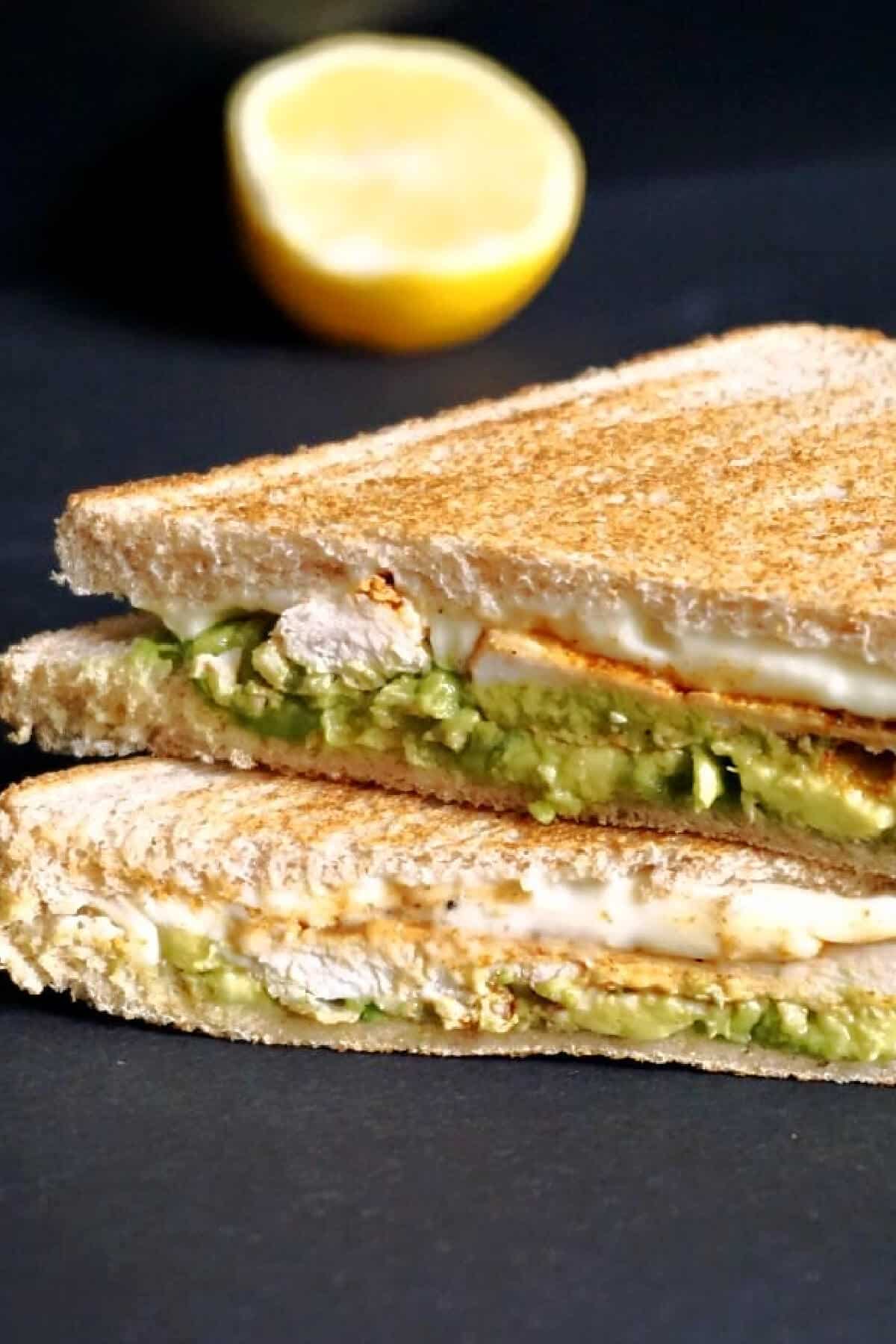 A stack of 2 sandwiches with avocado and chicken.