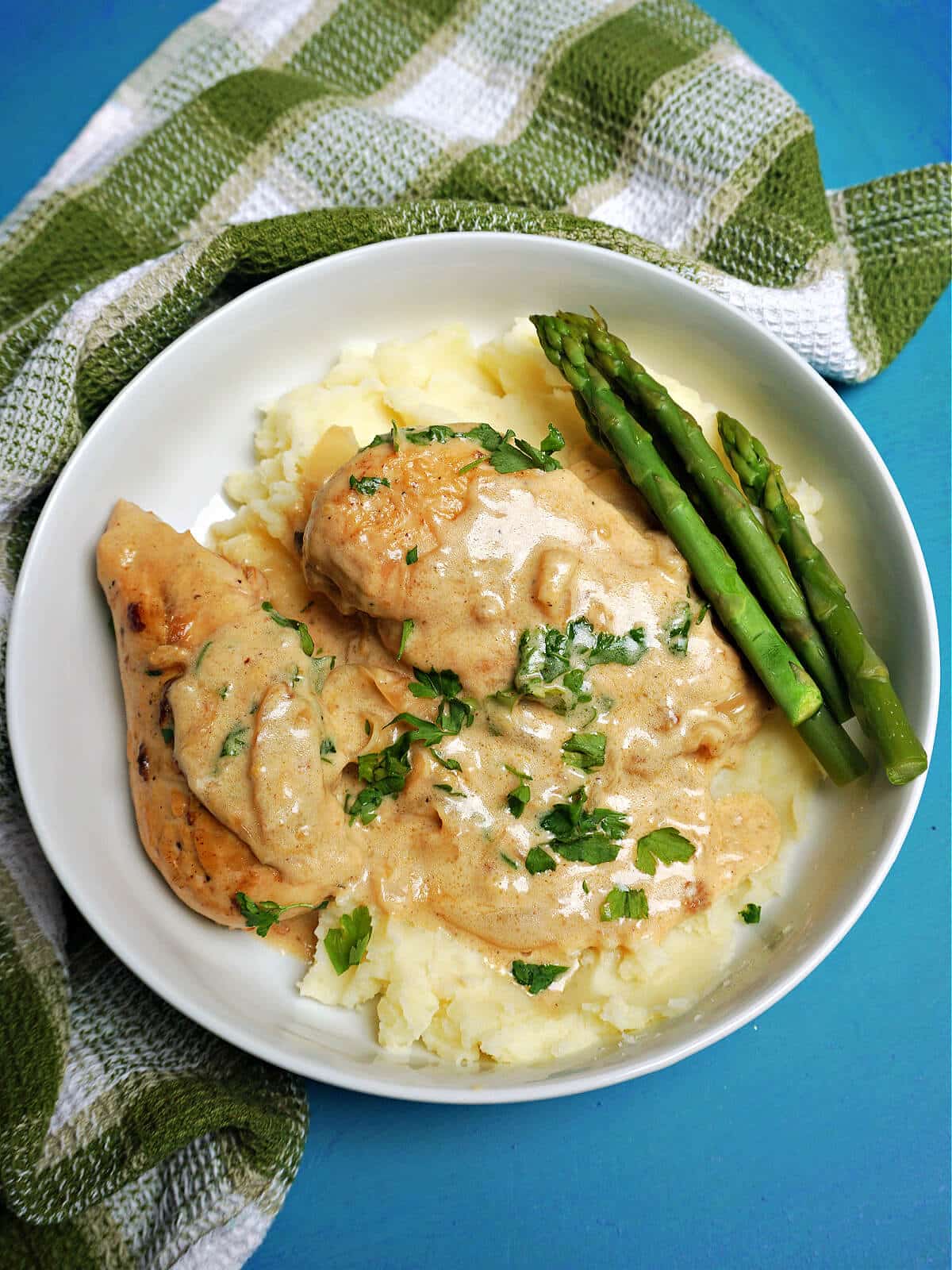 Overhead shoot of a white plate with mash 2 chicken breasts in creamy sauce and 3 asparagus spears.
