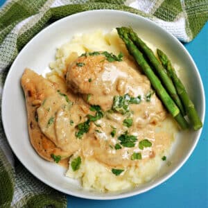 Overhead shoot of a white bowl with 2 chicken breasts in a sauce on a bed of rice and asparagus on the side
