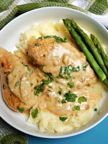 Overhead shoot of a white bowl with 2 chicken breasts in a sauce on a bed of rice and asparagus on the side