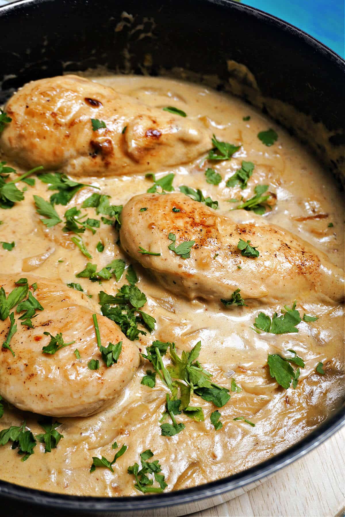 A cooking pot with 3 chicken breasts in a creamy sauce.