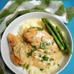 Overhead shoot of a white bowl with lemon chicken on a bed of mash with asparagus on the side