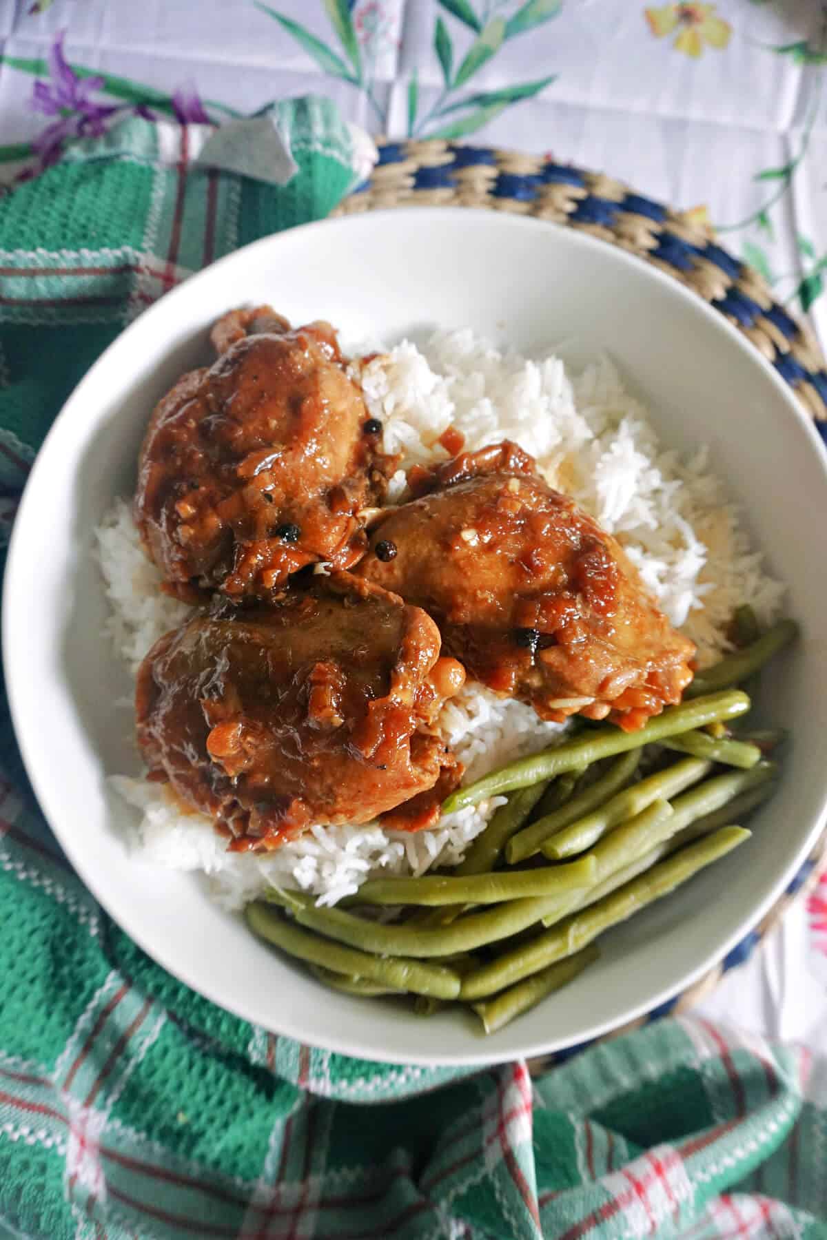 A white bowl with 3 chicken thighs over a bed of rice with green beans on the side.