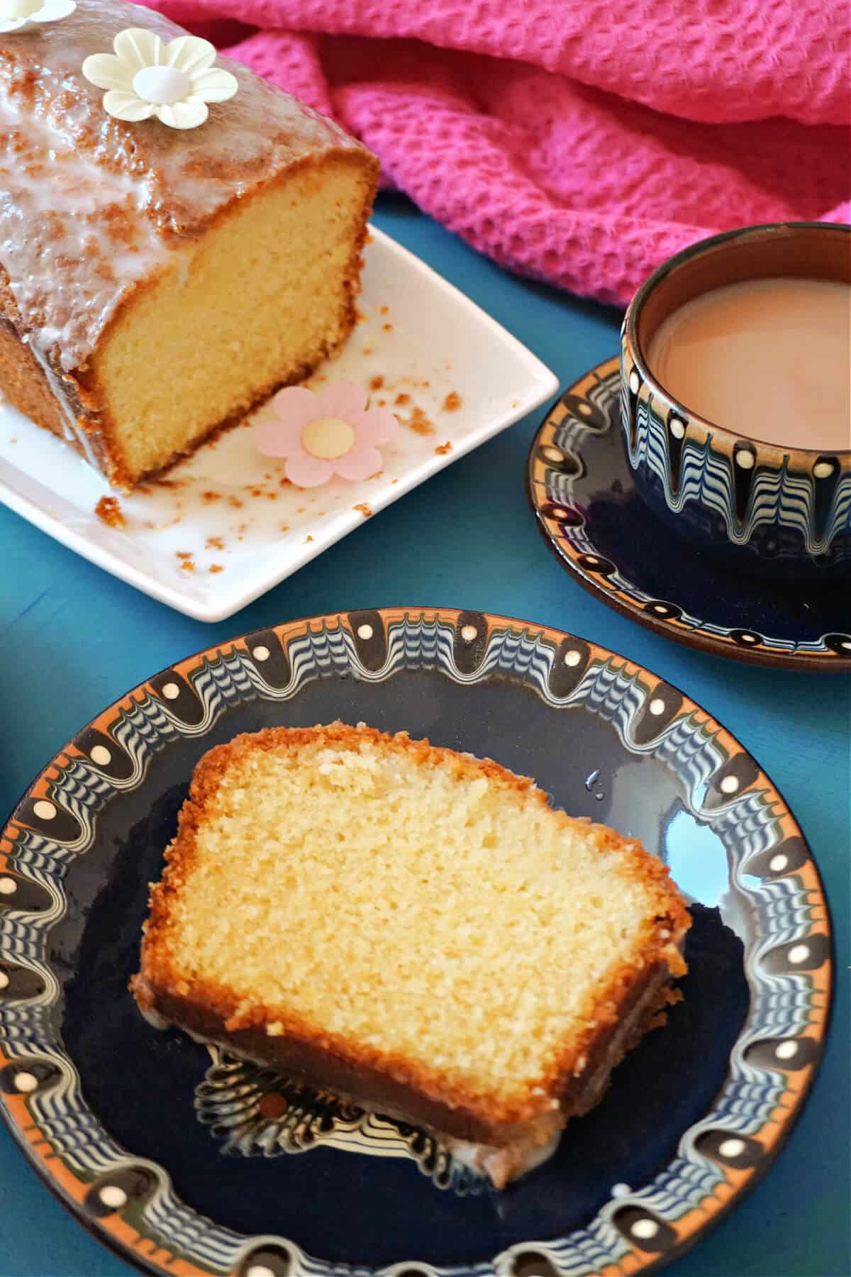 A slice of cake on a dark blue plate, a cup of tea and a white plate with more cake at the top