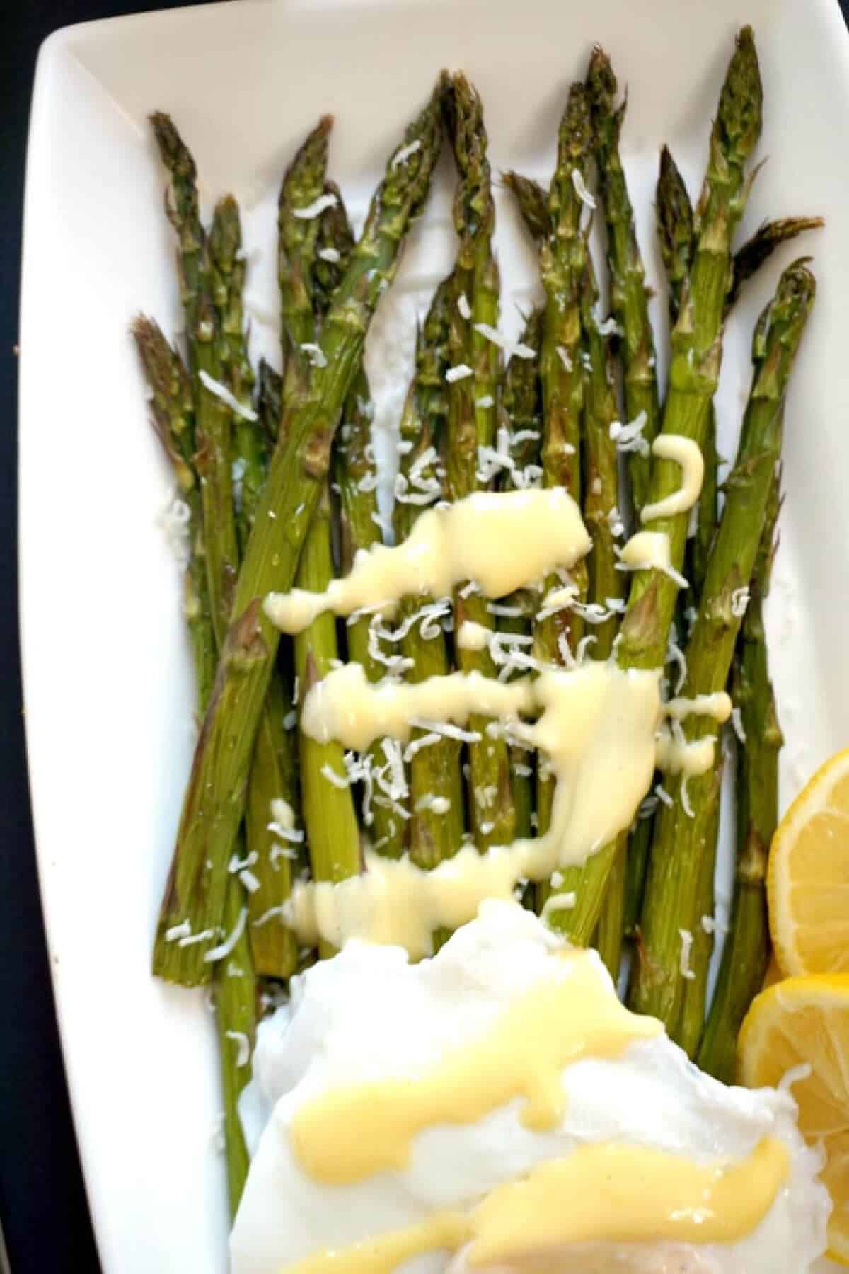 A white rectangle plate with grilled asparagus and hollandaise sauce.