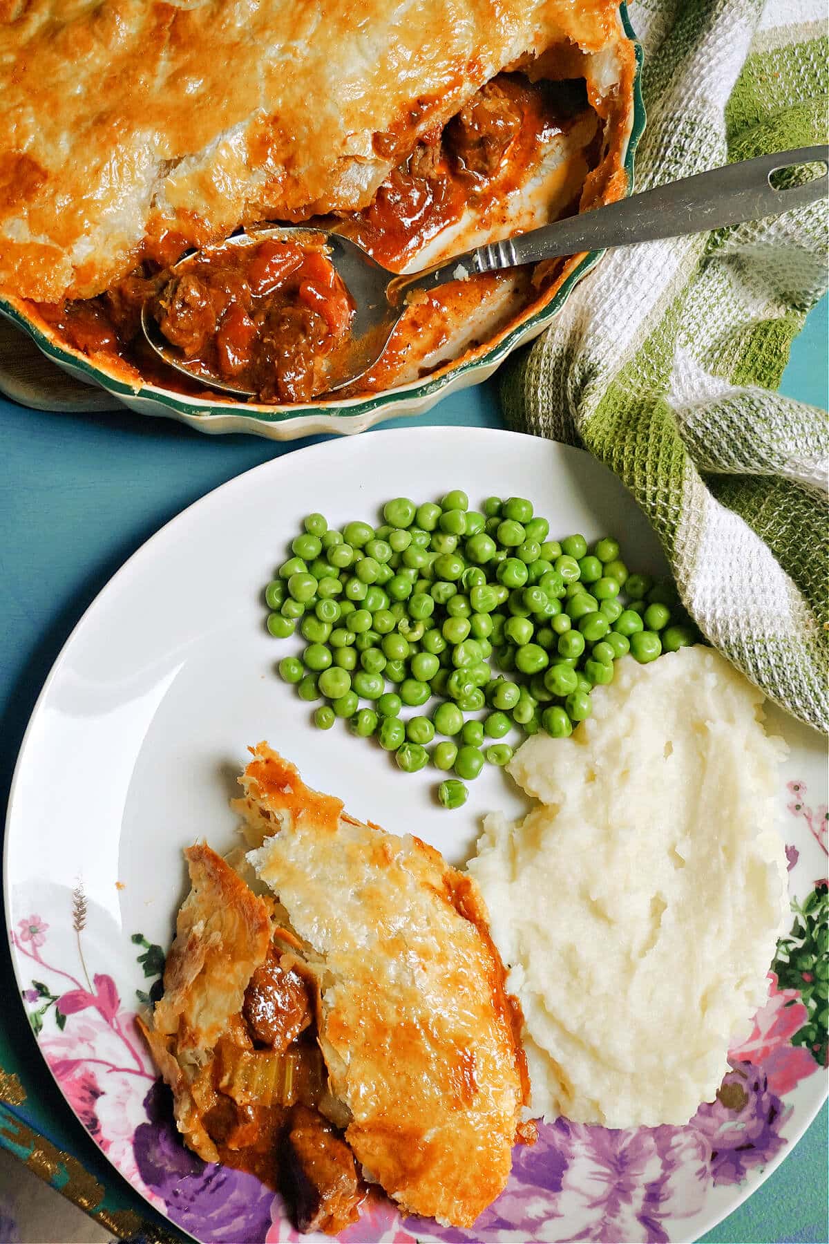 Overhead shoot of a white plate with a portion of pie, mash and peas, and a dish with more pie at the top.