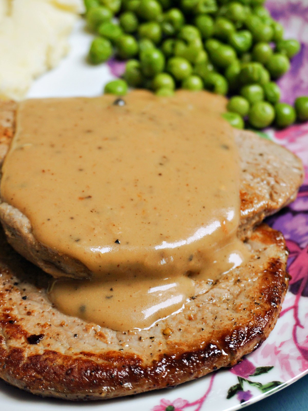 2 fillet steaks smothered in peppercorn sauce with peas at the top
