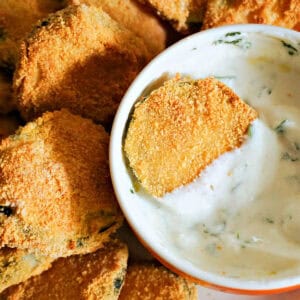 A white ramekin with yogurt sauce and a zucchini chip into it, and other chips around the ramekin.