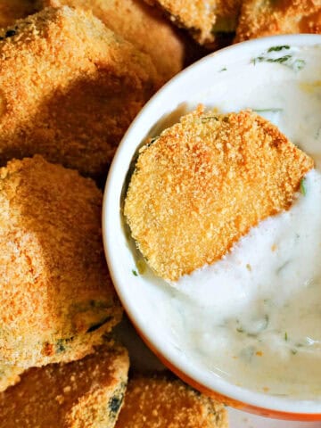 A white ramekin with yogurt sauce and a zucchini chip into it, and other chips around the ramekin.