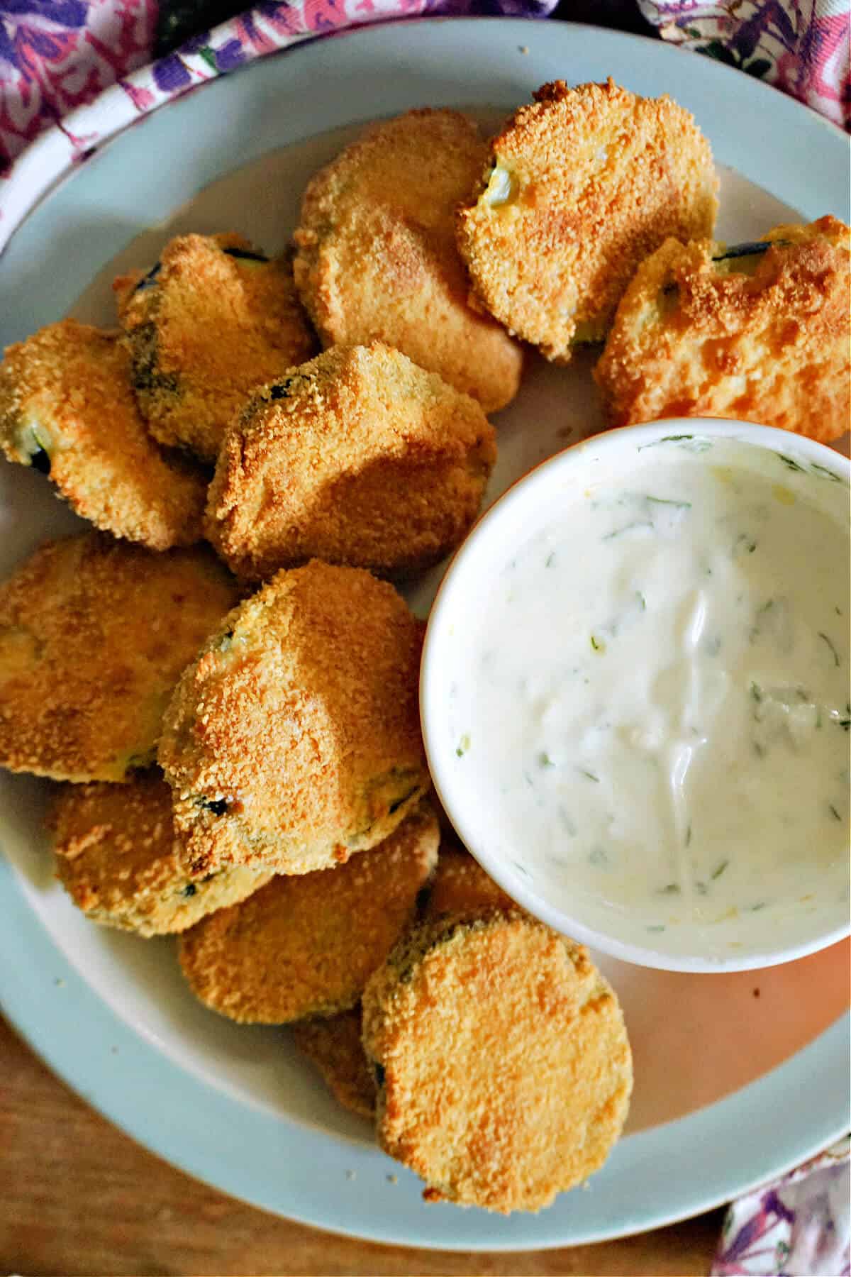 A white ramekin with yogurt sauce and zucchini chips arond it.