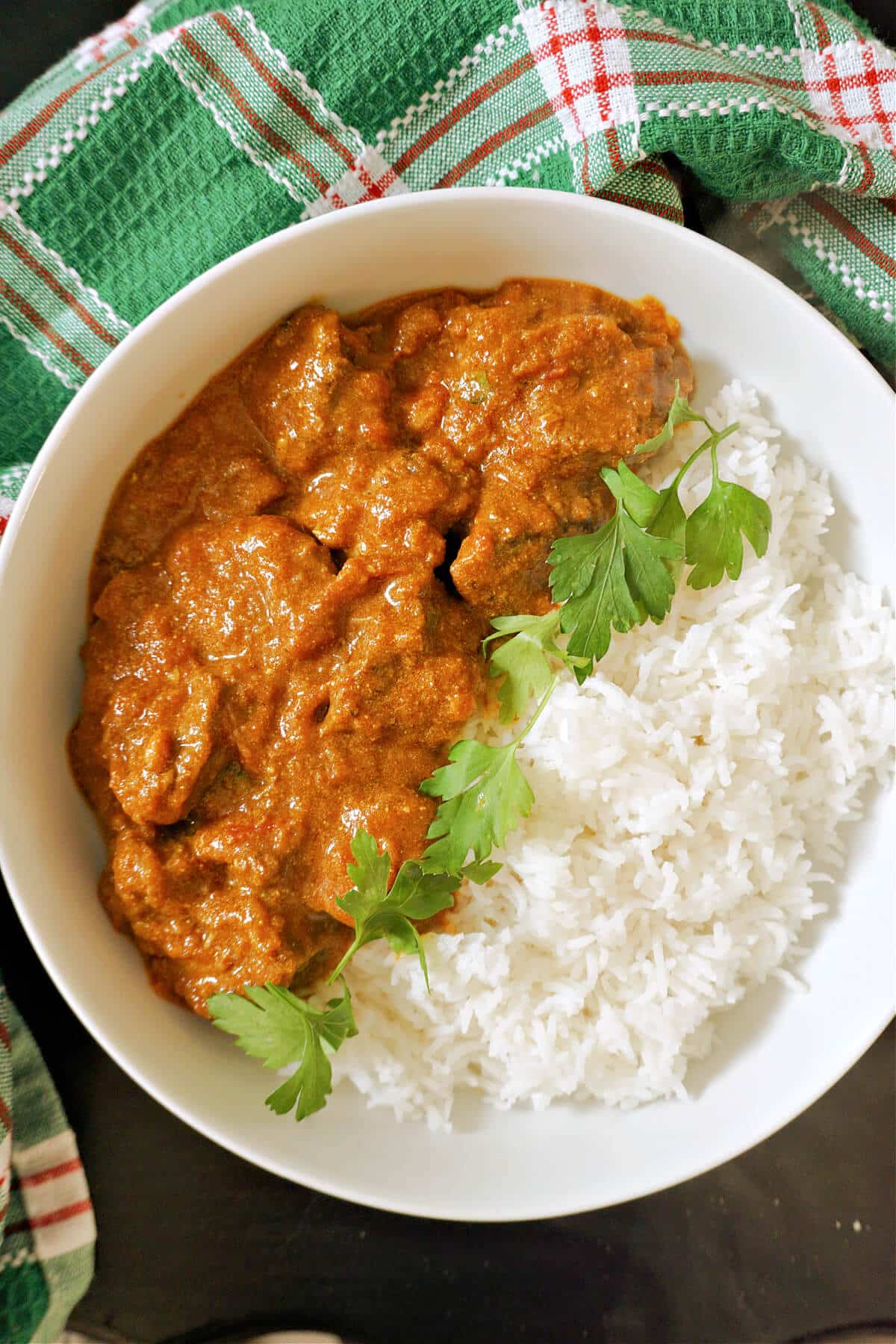 A white bowl with beef curry, rice and fresh parsley.