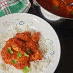 A white plate with chicken curry over a bed of rice