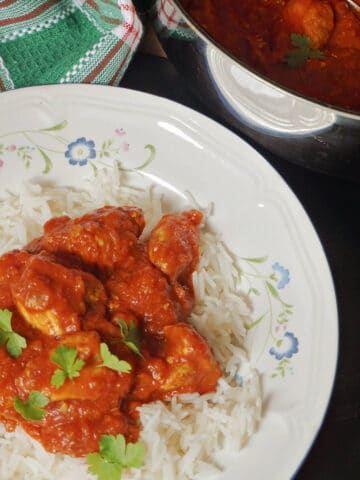 A white plate with chicken curry over a bed of rice