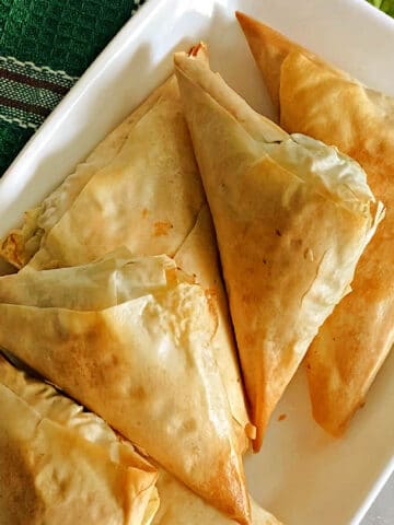 A white rectangle plate with Greek spanakopita triangles.