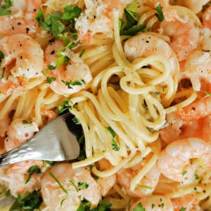 A fork twisting spaghetti on a bed of spaghetti and prawns garnished with chopped parsley.