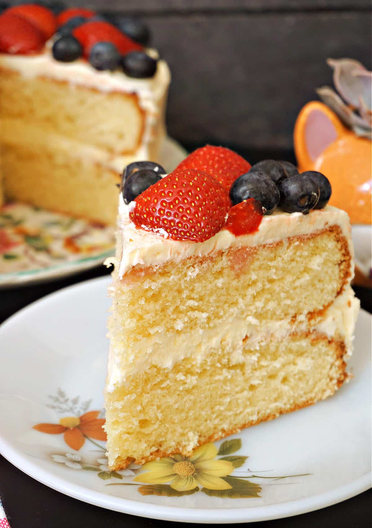 A slice of vanilla buttercream cake topped with blueberries and strawberries