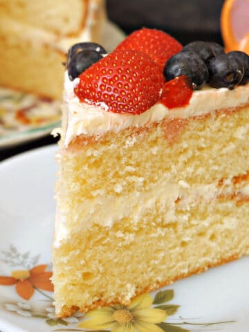 A slice of vanilla buttercream cake topped with strawberries and blueberries