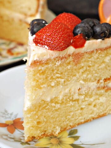 A slice of vanilla buttercream cake topped with strawberries and blueberries