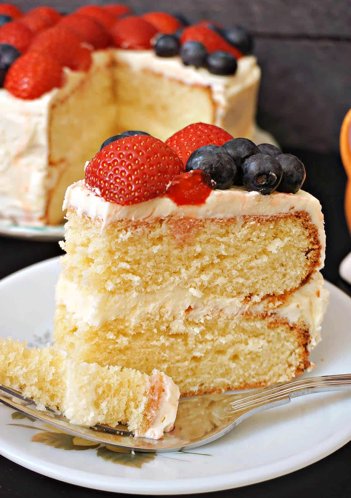 A slice of vanilla buttercream cake topped with strawberries and blueberries.