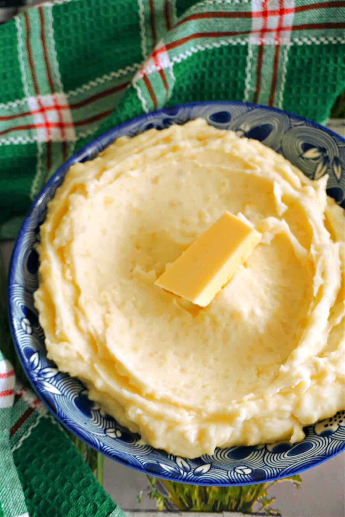 A plate with mashed potatoes and a cube of butter on top.