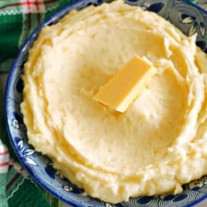 A bowl with mashed potatoes and a cube of butter on top.