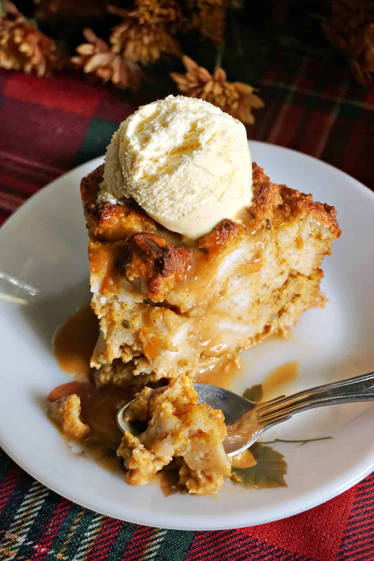 A white plate with a slice of pumpkin bread pudding topped with a scoop of vanilla ice cream.