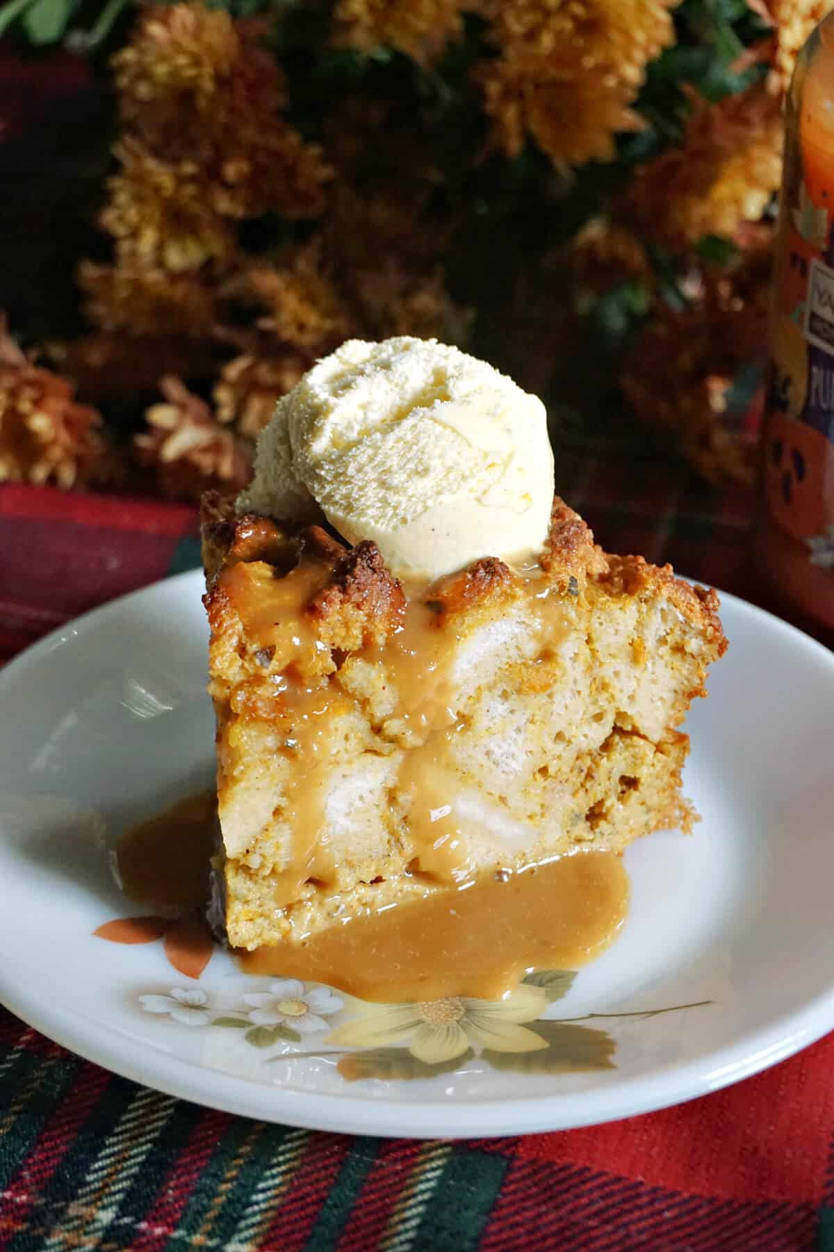 A slice of pumpkin bread pudding topped with butterscotch sauce and a scoop of ice cream.