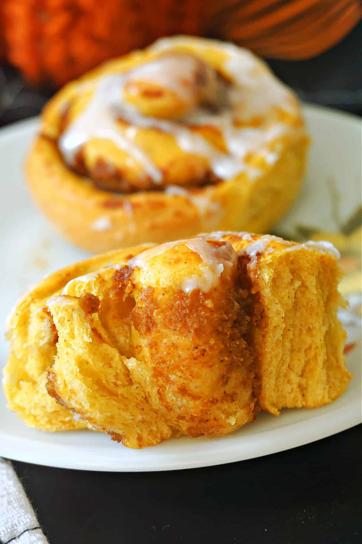 Half of a pumpkin cinnamon roll to show how fluffy it is and a whole roll in the background.