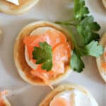 A plate with blinis topped with cream cheese, smoked salmon and fresh parsley.