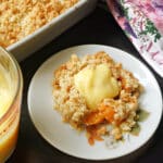 A plate with a portion of apricot crumble with custard on top.
