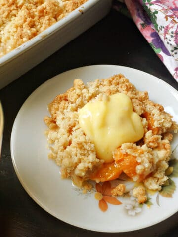 A plate with a portion of apricot crumble with custard on top.