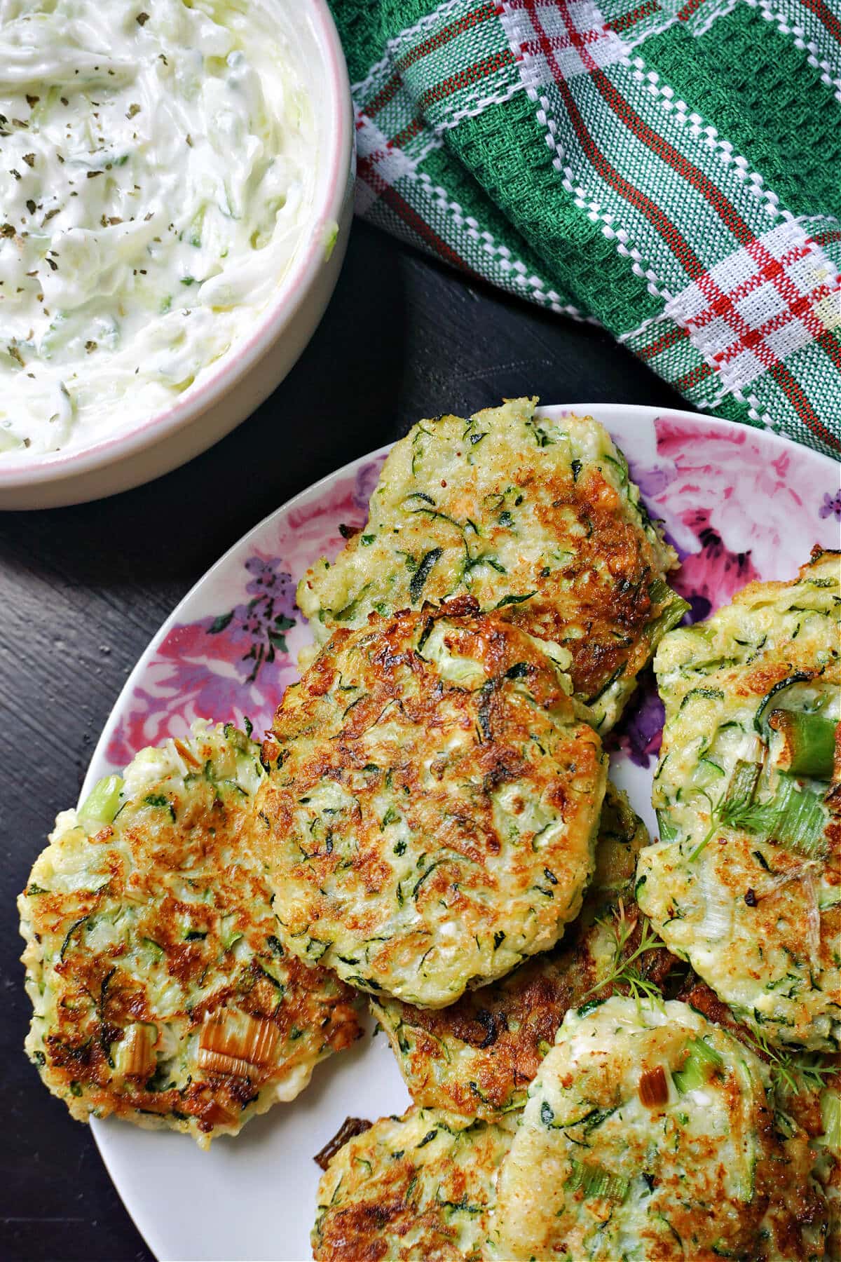 A plate with courgette fritters and a ramekin with tzatziki next to it.