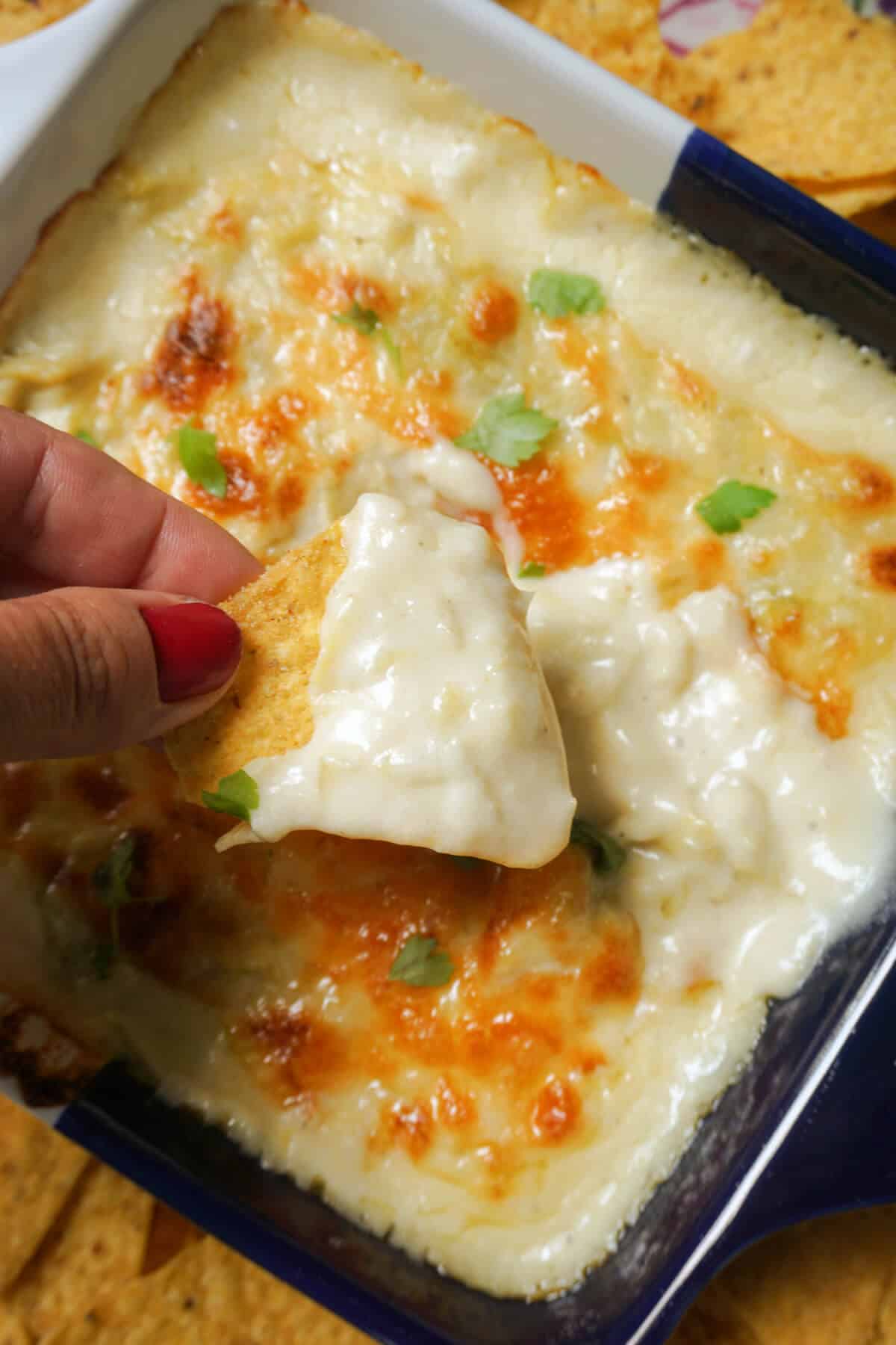 A hand scooping out some artichoke dip out of a dish with a tortilla chip