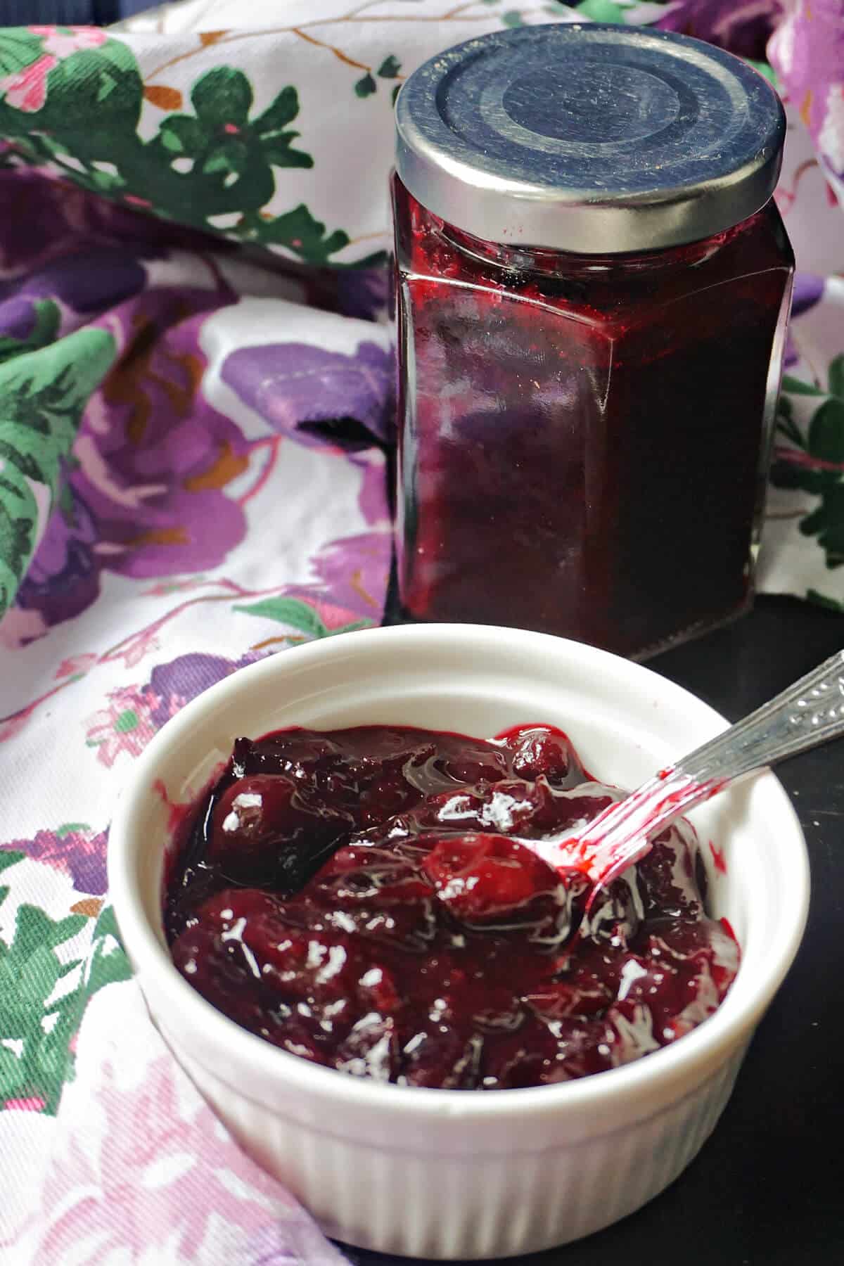 A white ramekin with damson jam and a jar with more jam in the background.