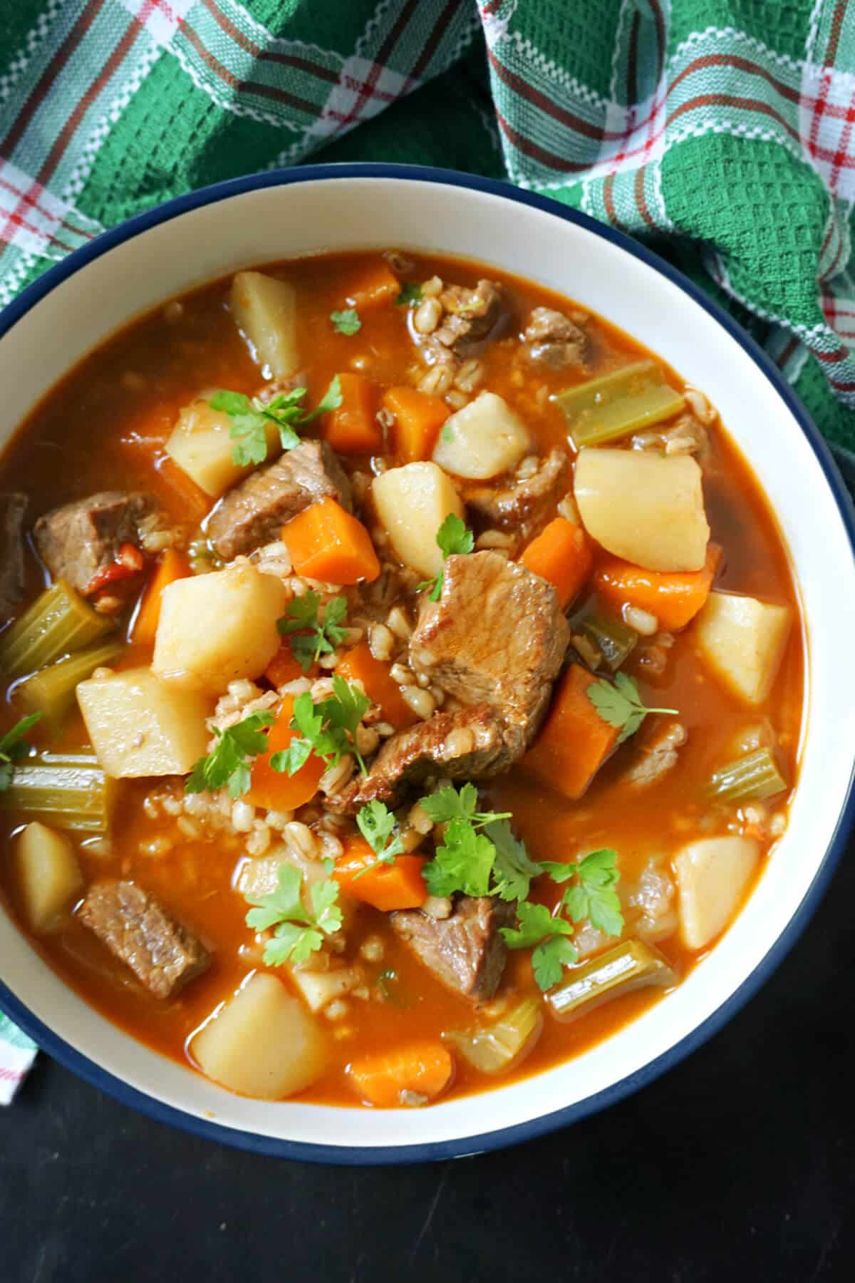 A white bowl with beef, barley and vegetables soup.